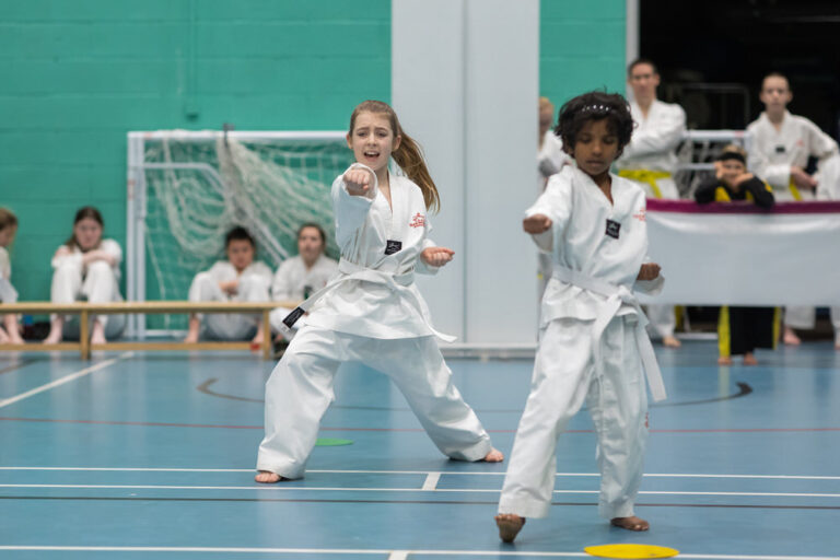 Two students in white belts performing punches in unison during their grading patterns demonstration.